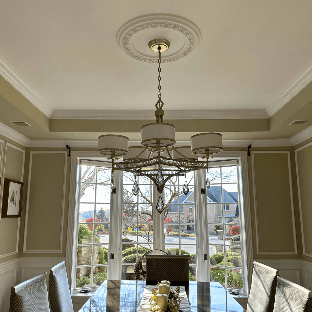 Elegant dining room with a large chandelier and view of houses through tall windows.