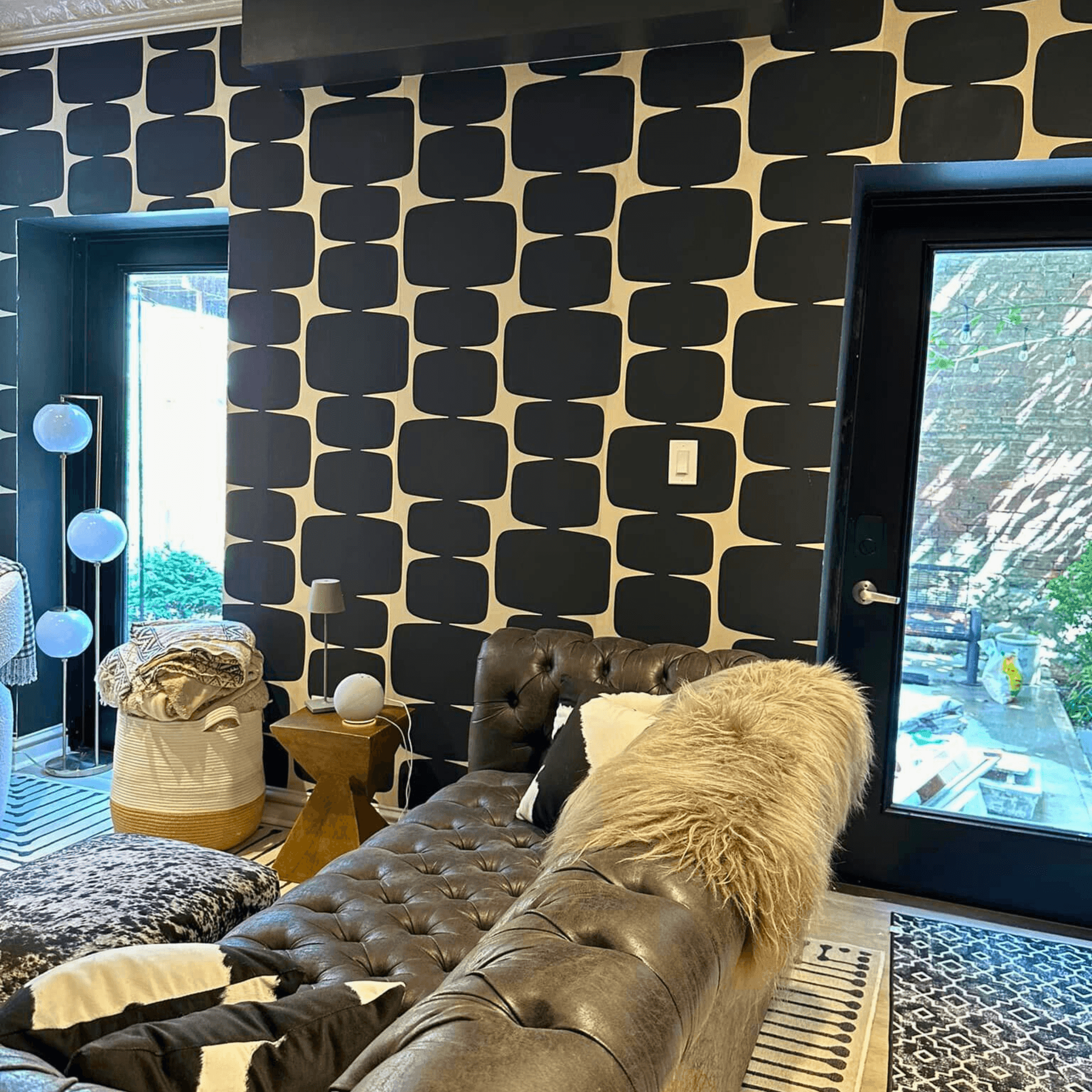 Living room with patterned black and white wall, leather sofa, and window overlooking a garden.